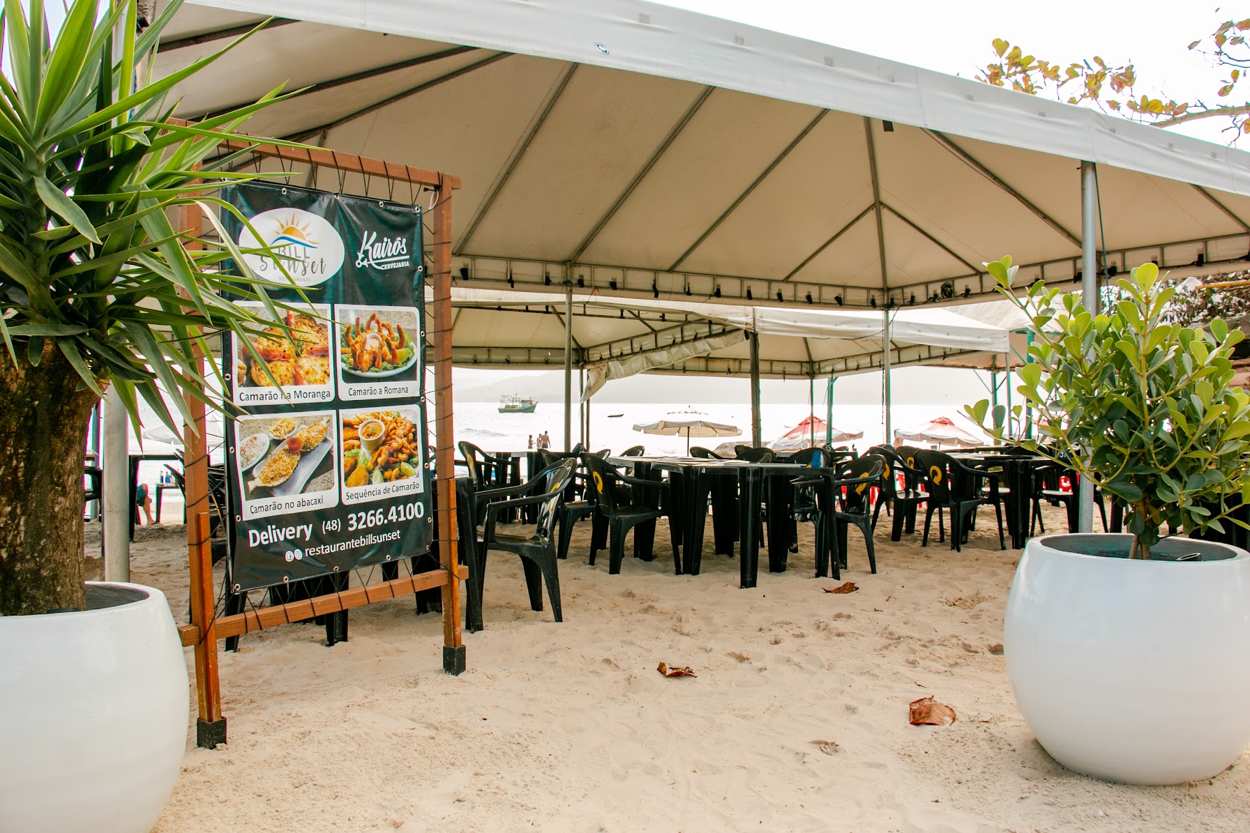 Ambiente do Bill Sunset com mesas na areia e vegetação